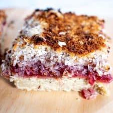 One raspberry and coconut tart on a wooden platter.