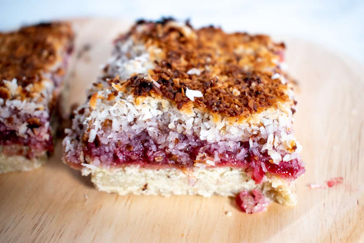 Two vegan raspberry and coconut slices on a wooden platter.