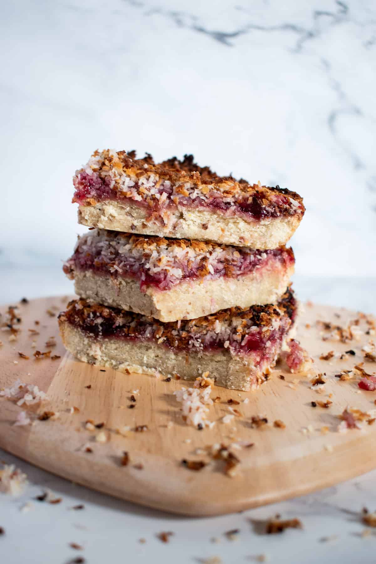 Three stacked raspberry and coconut slices on a wooden platter.