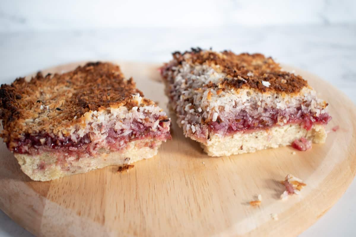 Two vegan raspberry and coconut slices on a wooden platter.