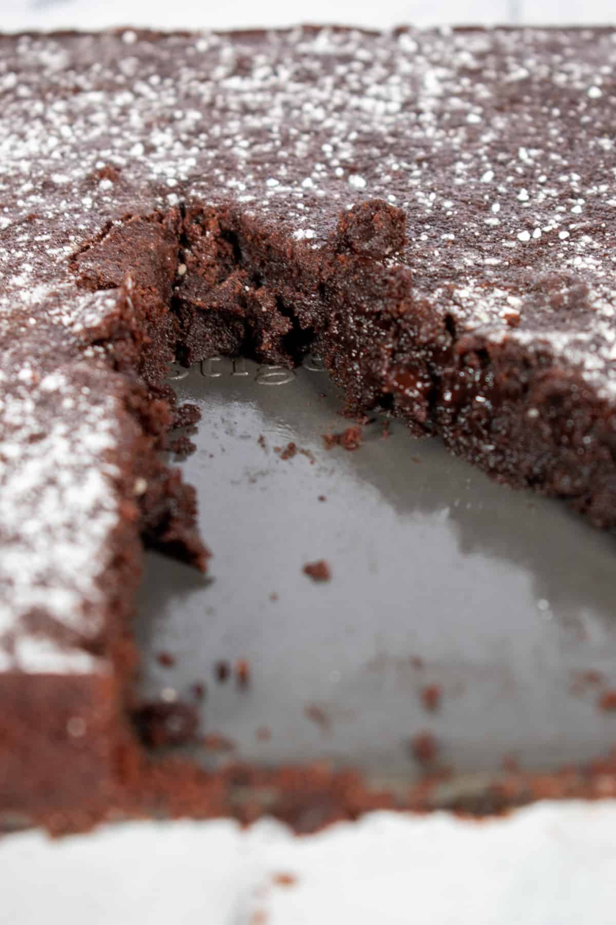 A vegan chocolate fudge cake with a slice missing.
