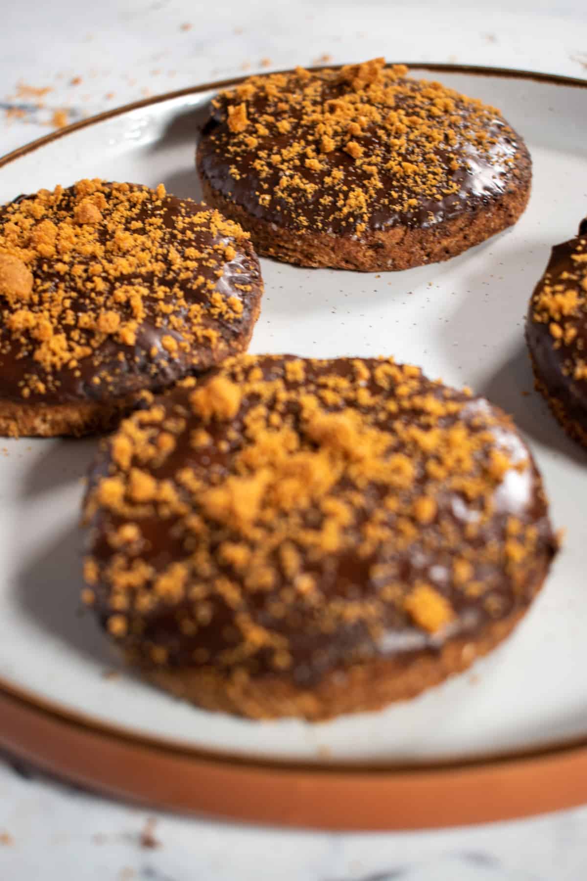 Four chocolate digestives on a brown and white plate.