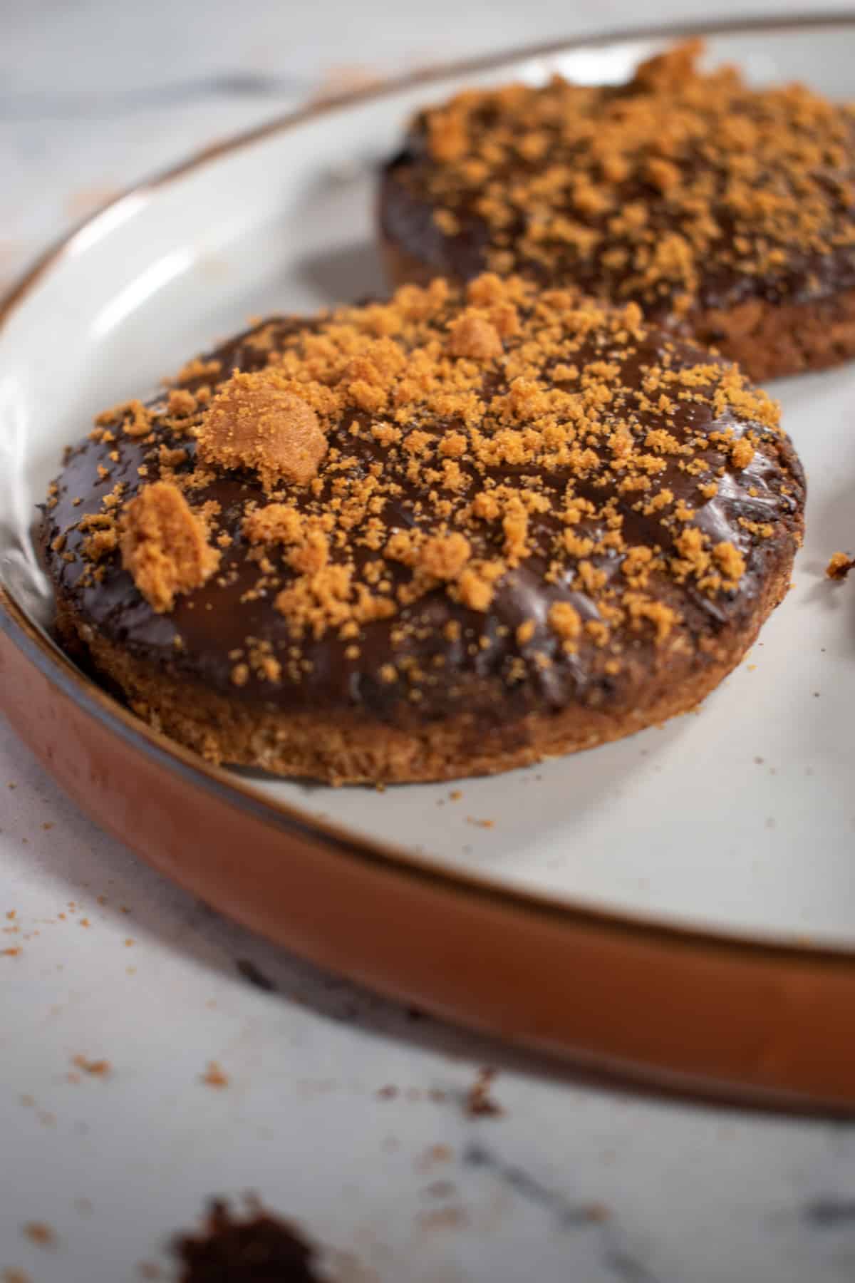 Two chocolate digestives on a brown and white plate.