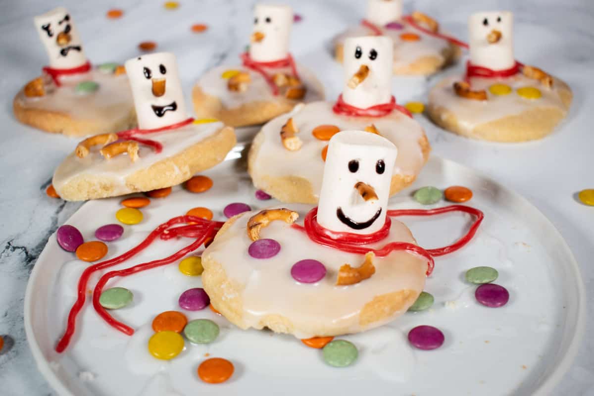 Decorated vegan melted snowman cookies on a white plate.