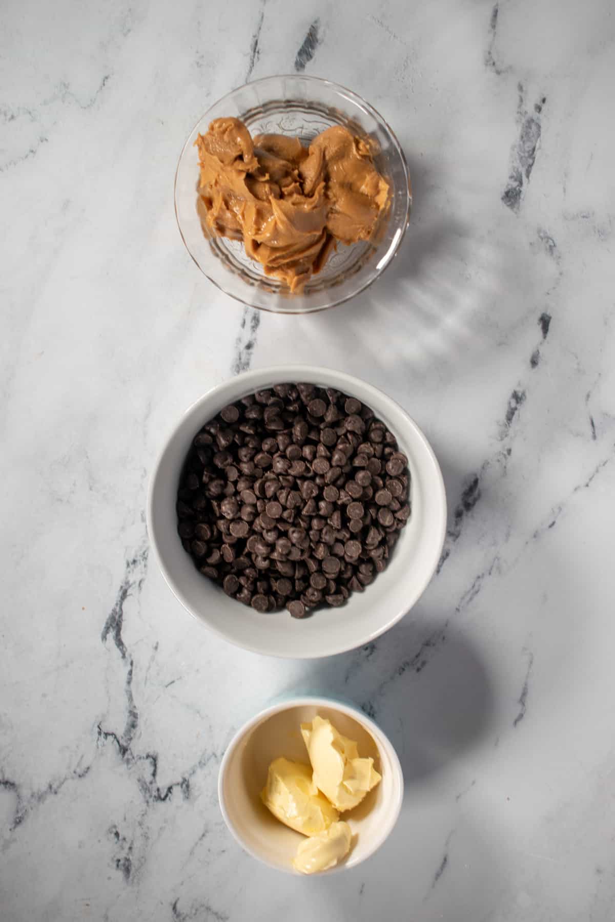 An aerial shot of a the ingredients needed to make vegan chocolate peanut butter fudge. Peanut butter, dairy free chocolate chips and vegan butter.