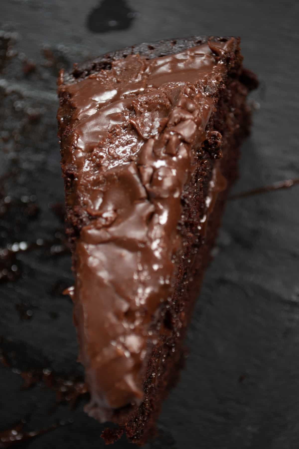 An aerial shot of a single slice of chocolate ganache cake. The ganache topping is shiny. 