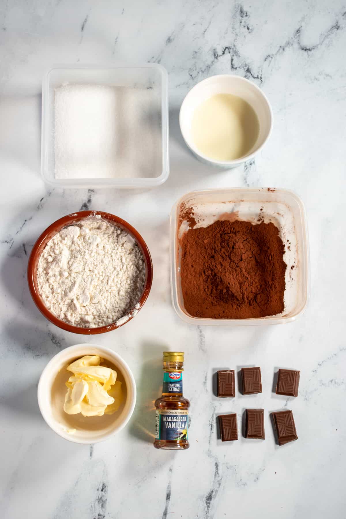 An aerial shot of the ingredients needed for my vegan chocolate mug cake recipe. Flour, sugar, cocoa powder, vegan butter, plant milk, vanilla and vegan chocolate.