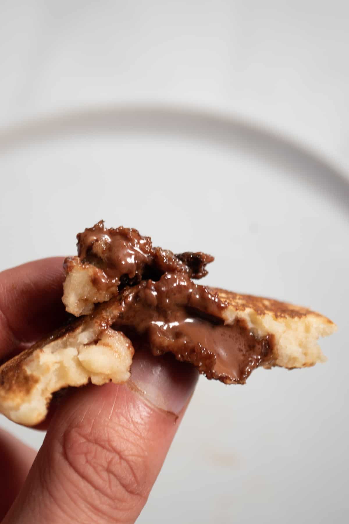 A hand showing a torn pancake to the camera. Chocolate oozing out.