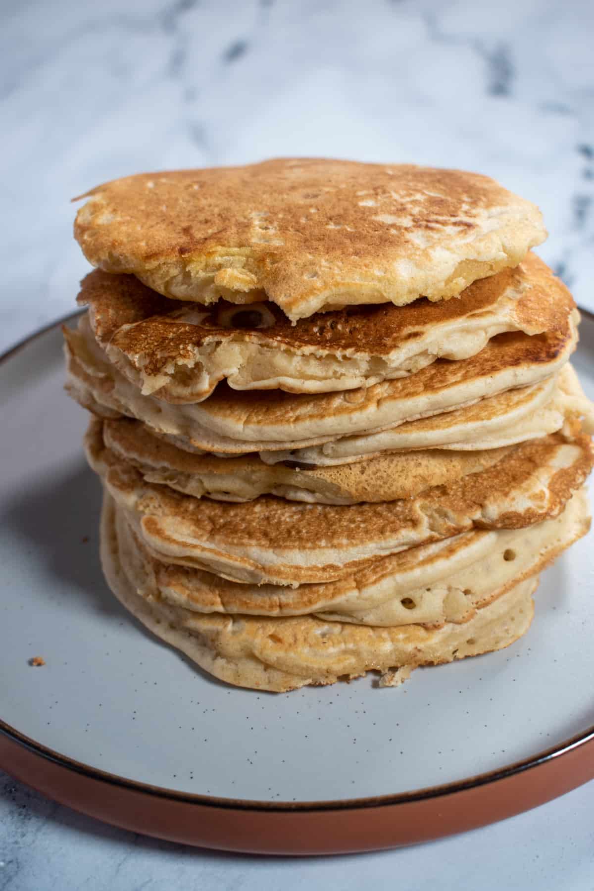 A stack of vegan pancakes with any toppings on a white and brown plate. 