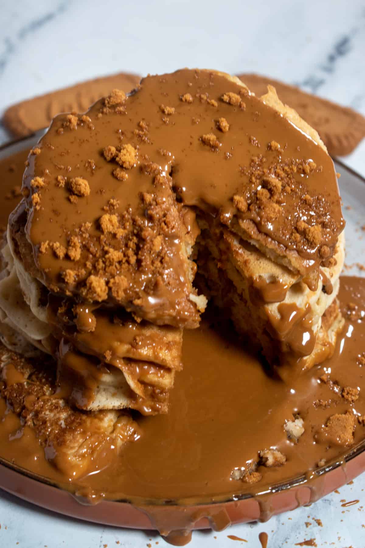 A gooey stack of vegan pancakes. They're covered with melted Biscoff spread and Biscoff cookie crumbs. 