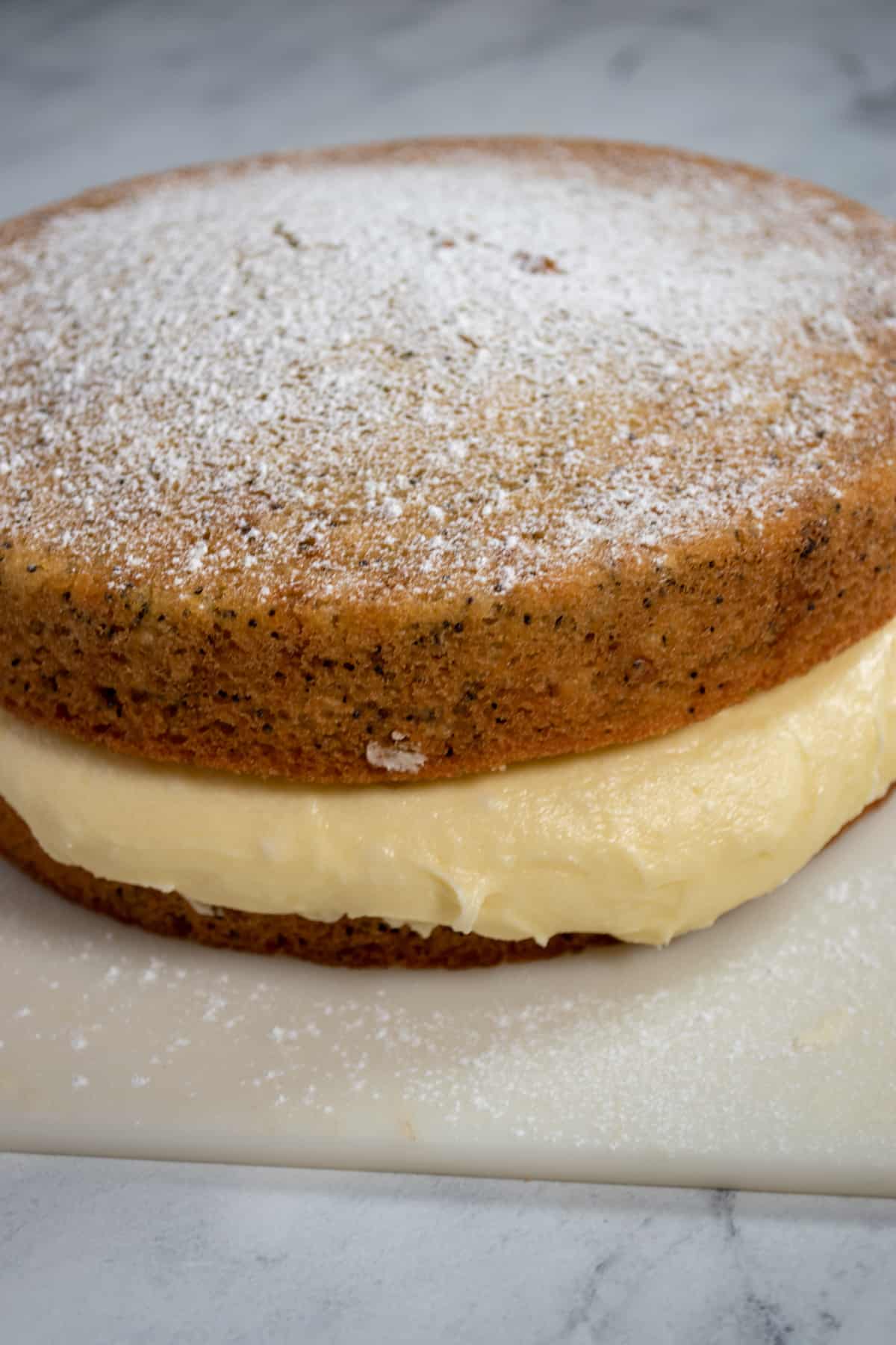 A whole, unsliced lemon poppy seed cake. Lemon buttercream oozing out. Powdered sugar on top. 