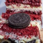 A large slice of red velvet cake with a whole oreo placed on top.