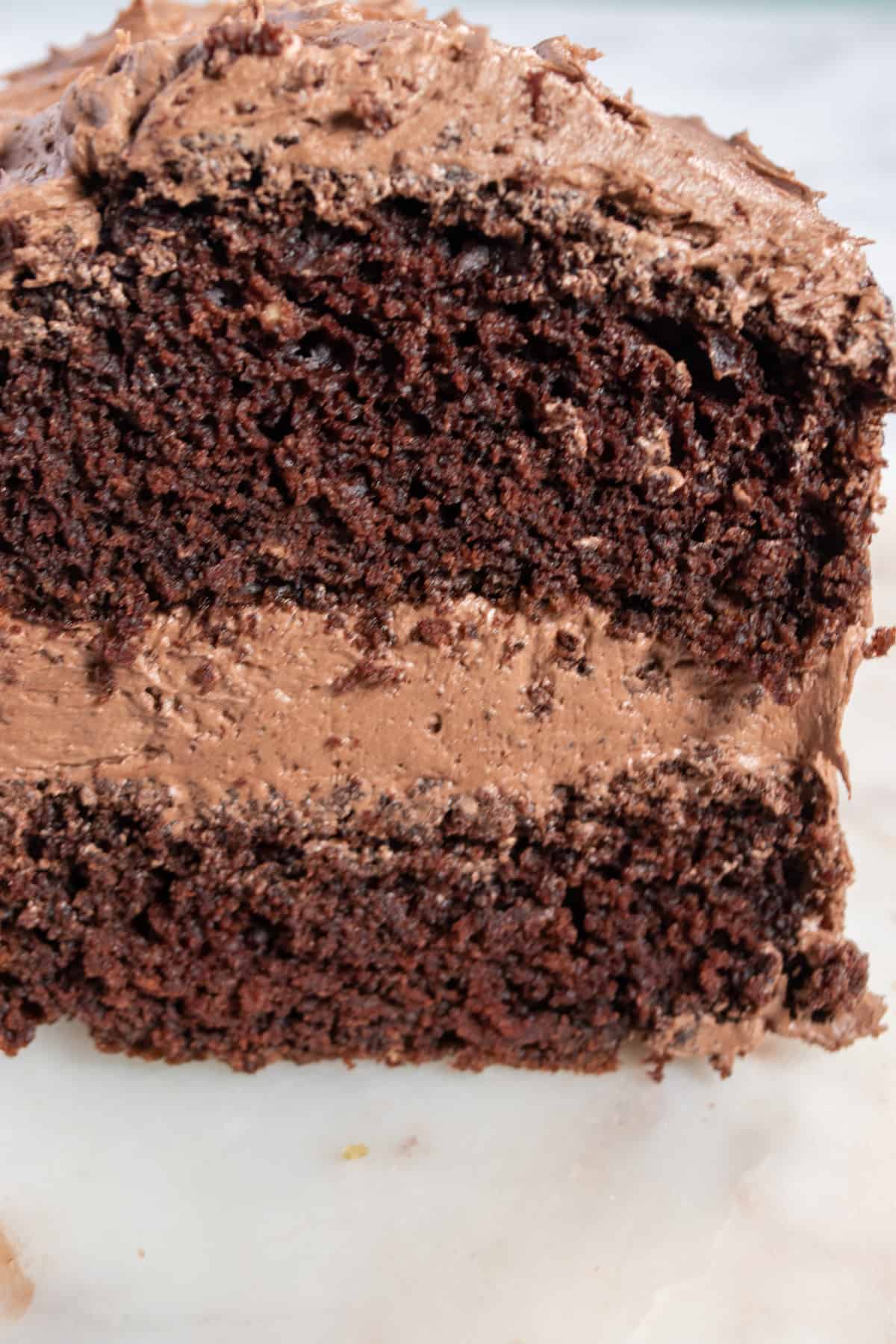 An entire eggless chocolate cake loaf with the front sliced. There is lots of frosting in the center and on top.