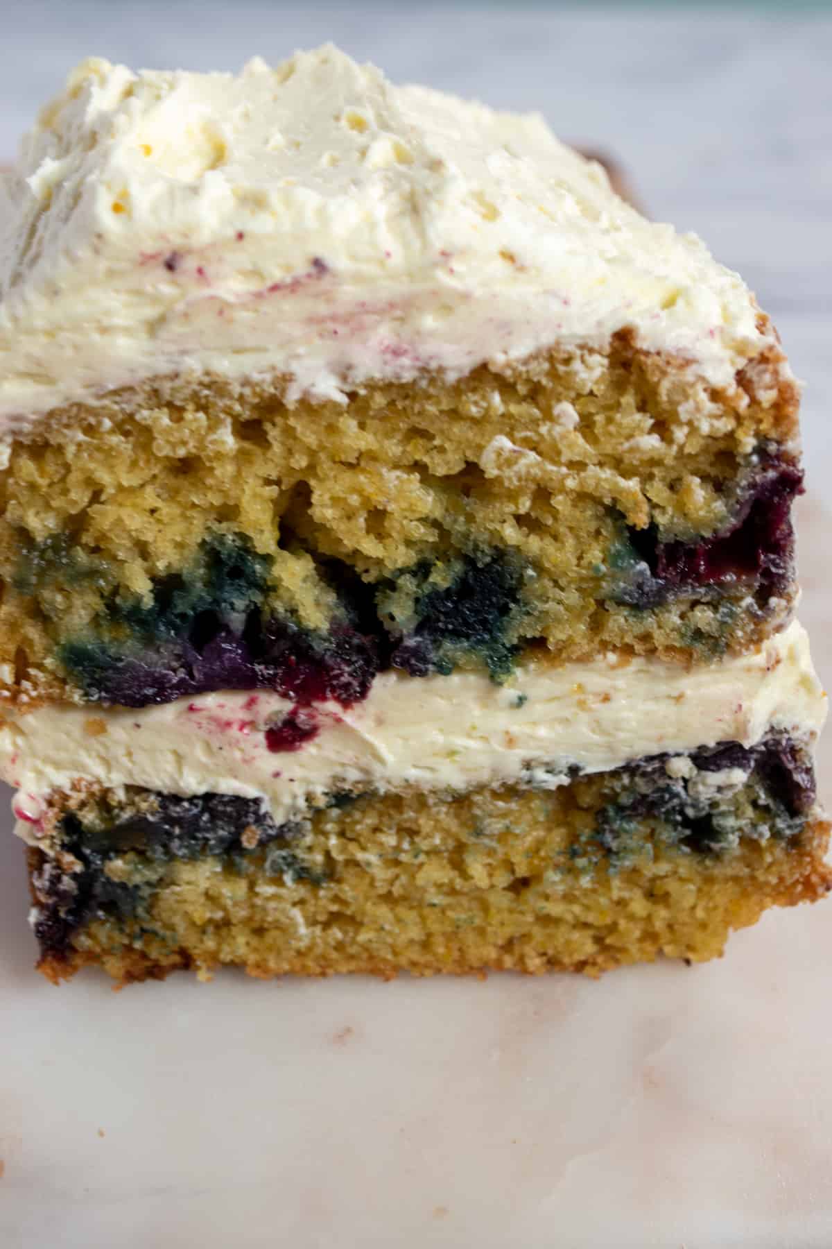 A whole loaf of orange blueberry cake which is filled with juicy blueberries and topped with vanilla buttercream. The front has been sliced off, revealing the moist texture. 