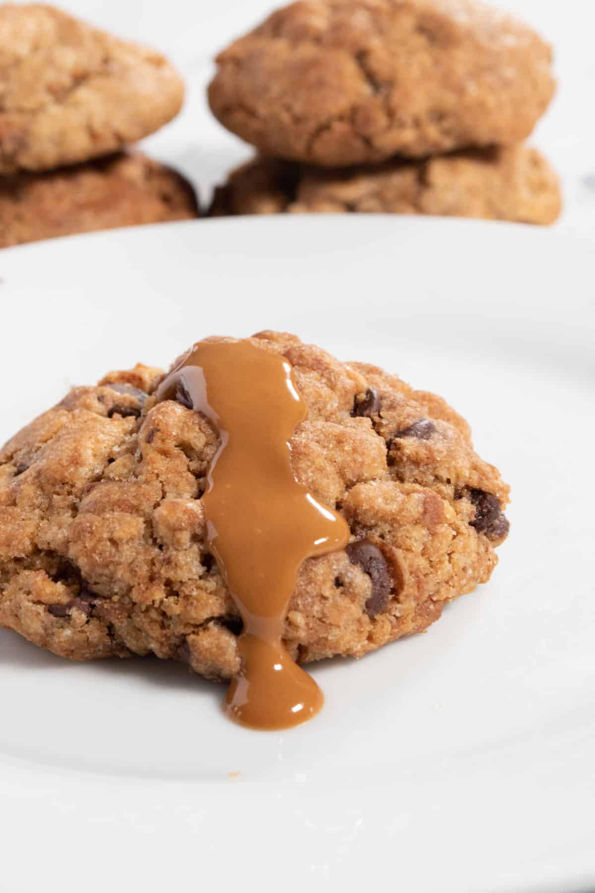 A single cookie in the foreground with melted biscoff spread dripping down it. More vegan biscoff cookies are stacked in the background.