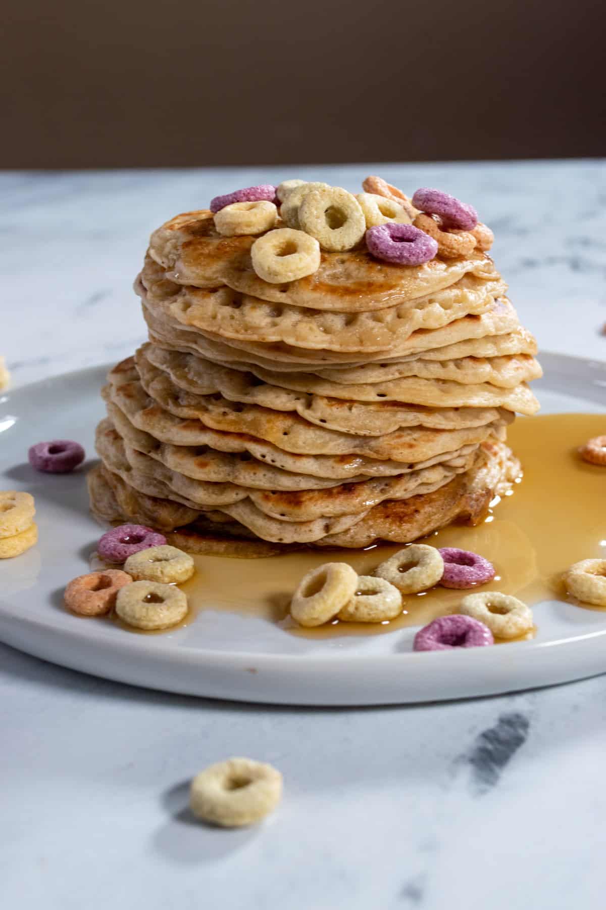 A stack of pancakes with cereal on top on a white plate. They're so soft and golden.