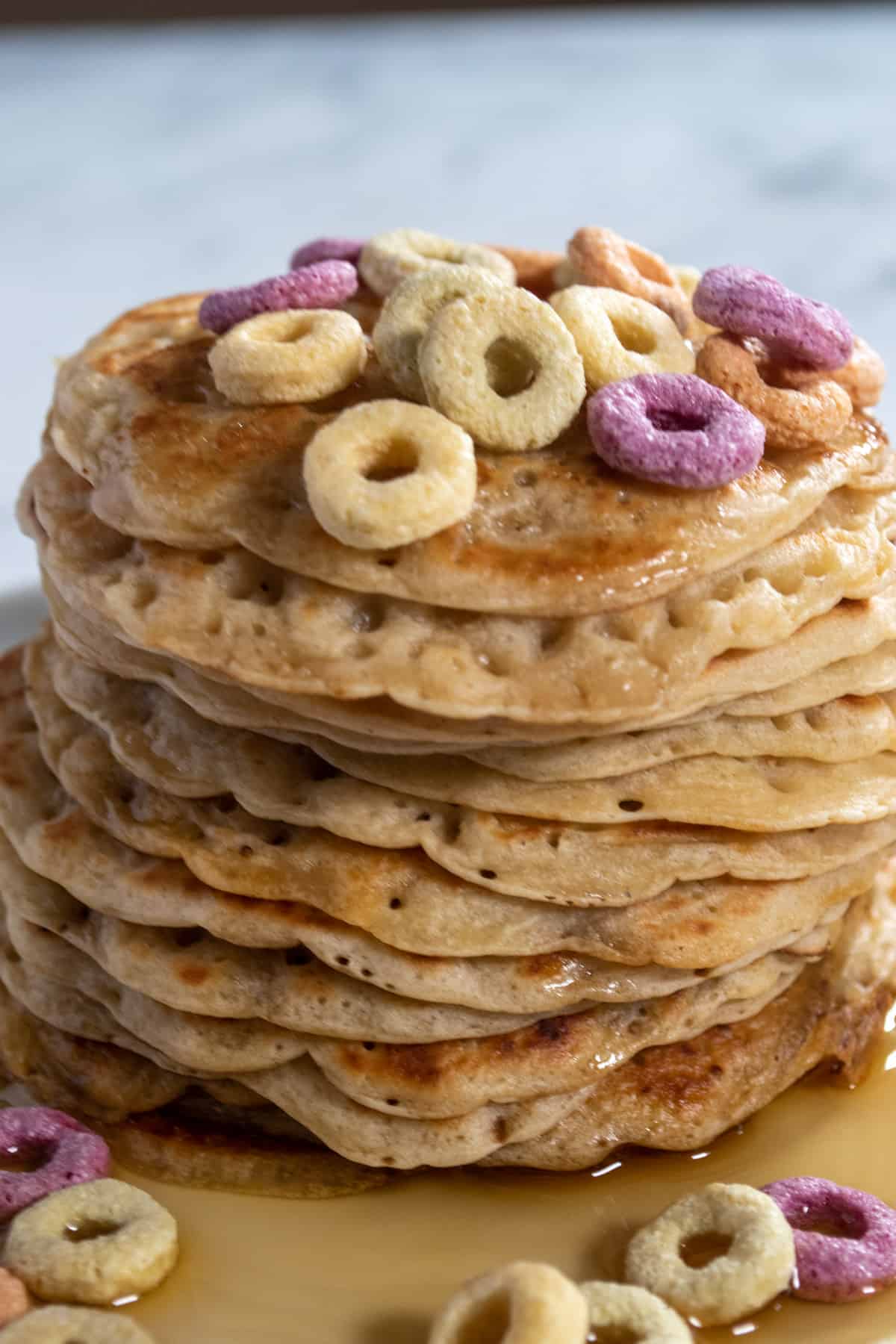 A stack of brown sugar pancakes. Sat in a small pool of maple syrup. They're topped with colorful cereal.