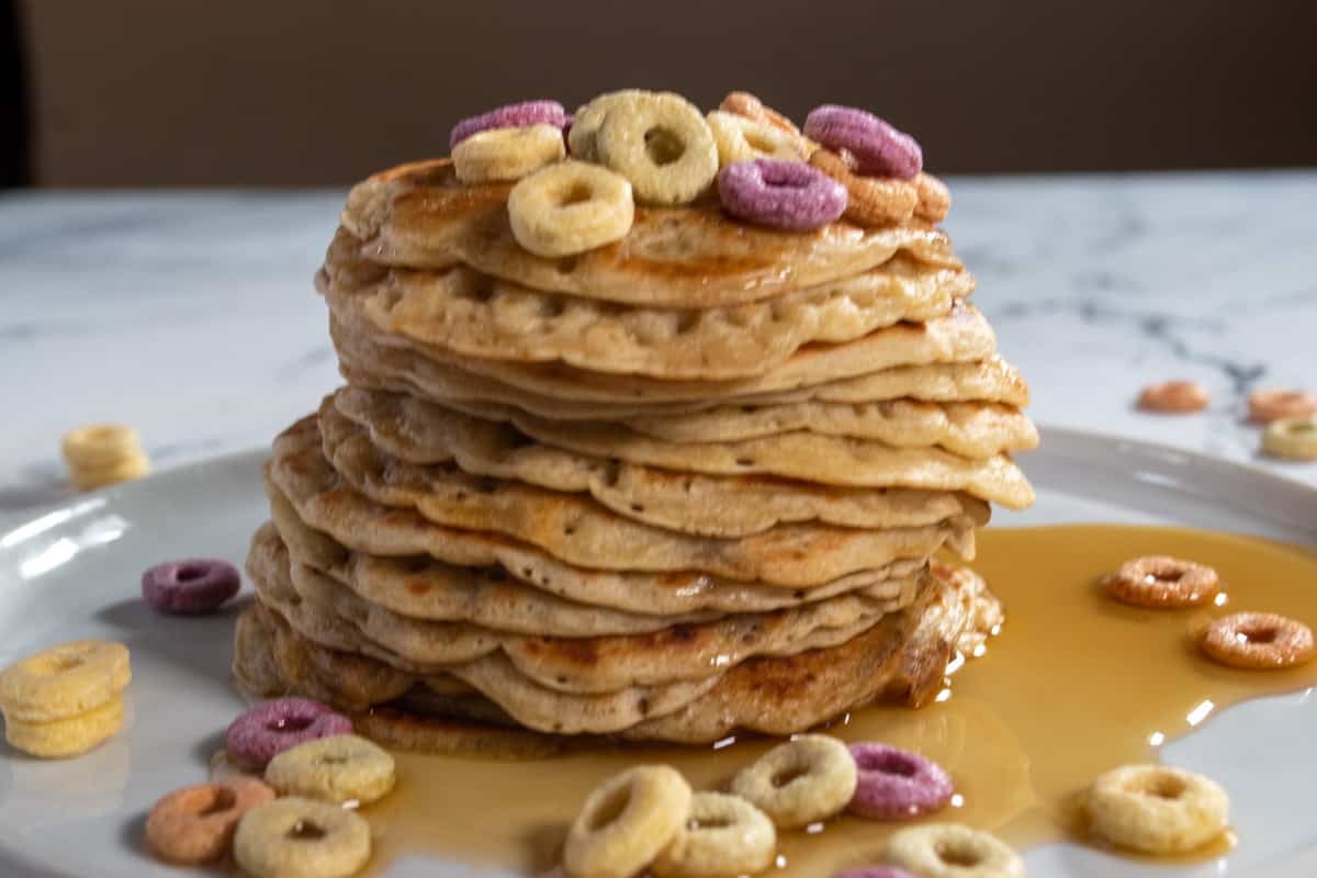 A stack of brown sugar pancakes, covered in maple syrup and topped with colourful cereal hoops. 