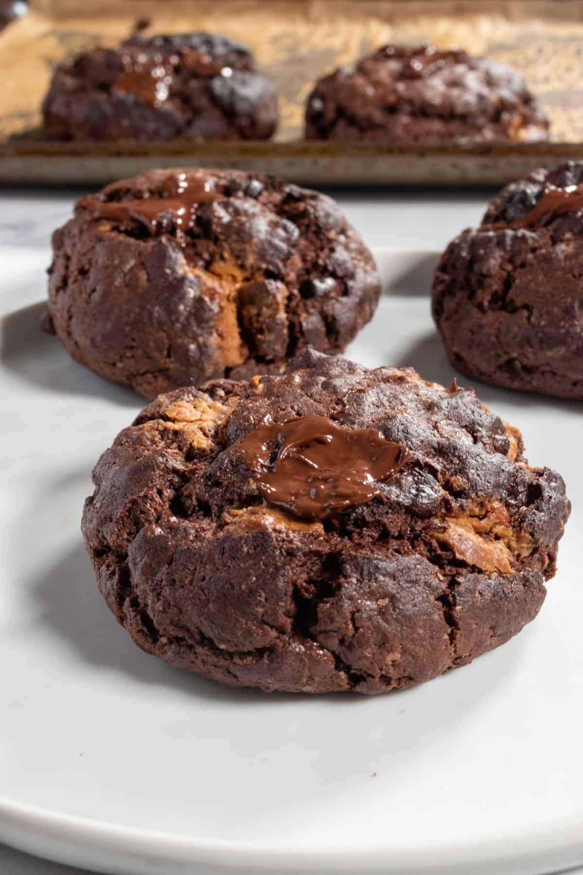 A close up shot of an extra large vegan chocolate brownie cookie. More cookies in the background.