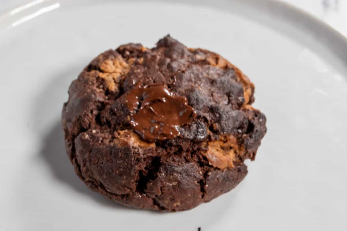 A large, round vegan chocolate brownie cookie on a clear white plate.