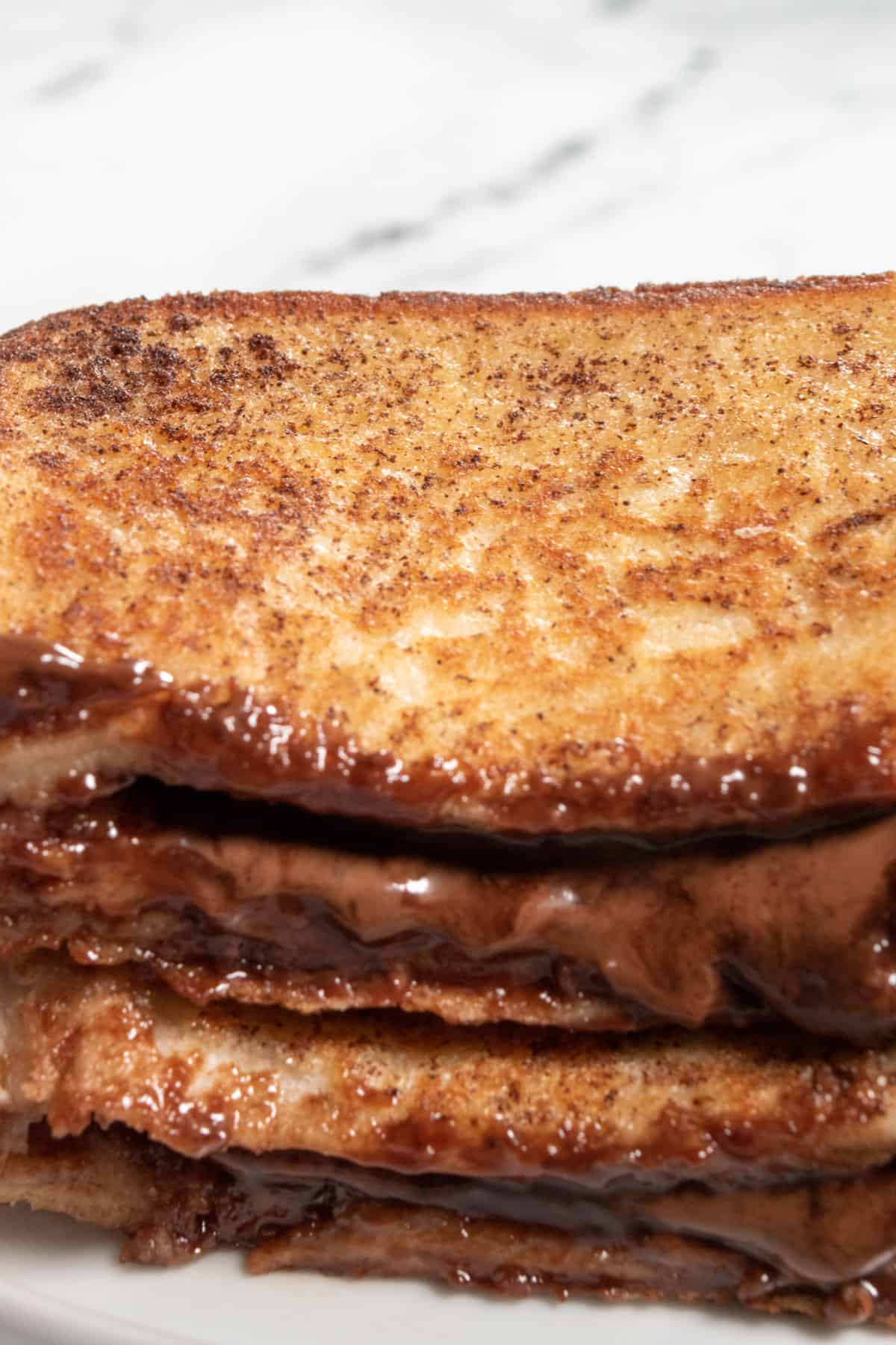 Stacked french toast on a white saucer. It looks crispy and golden. 