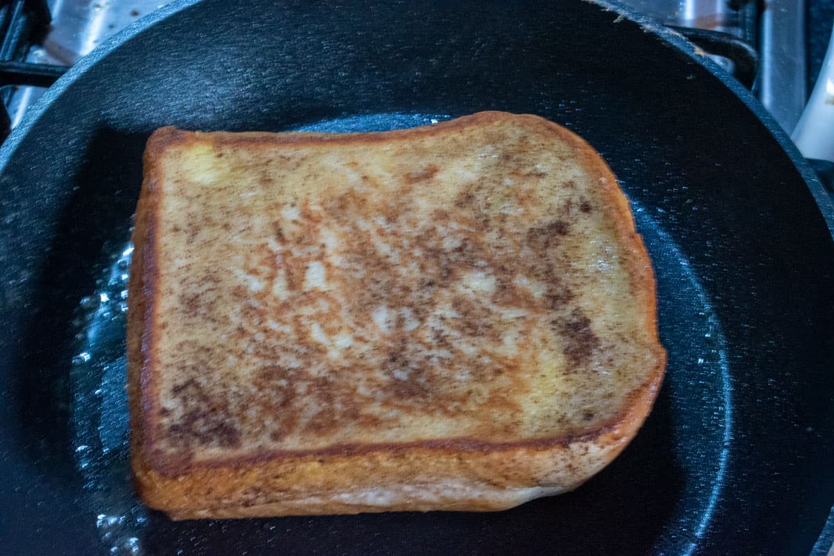 A shot of a cooked, golden brown vegan chocolate french toast in a black frying pan.