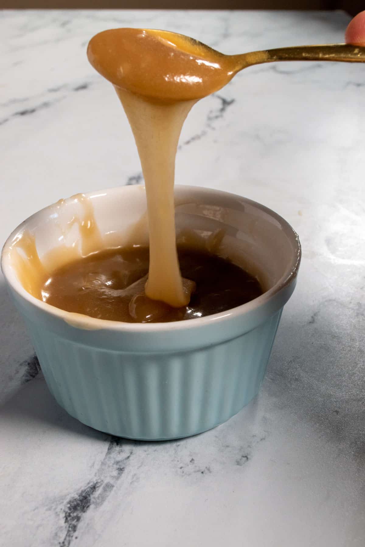 Vegan dulce de leche being drizzling into a ramekin from a golden spoon. 