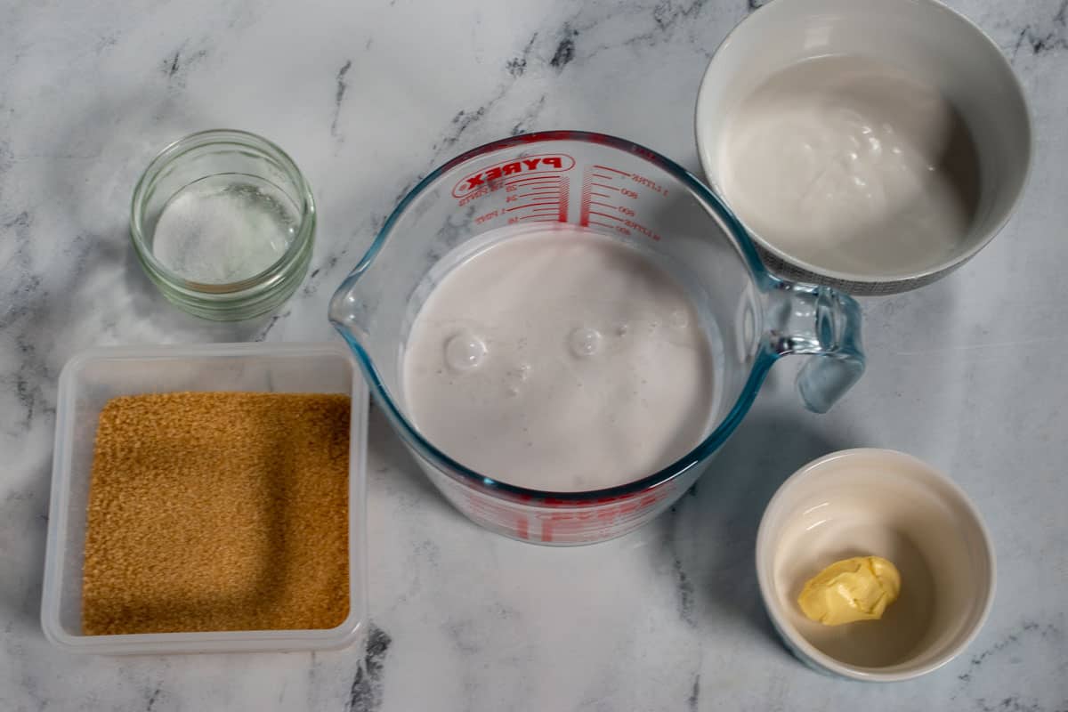 The five ingredients that you will need to make my vegan dulce de leche caramel laid out neatly over a white, marble background.