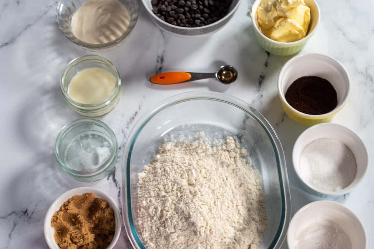 The ingredients needed to make espresso chocolate chip cookies laid out neatly over a white, marble background.