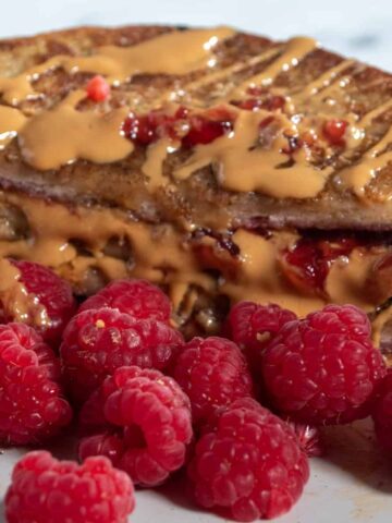 A colourful shot of my peanut butter and jelly french toast. It is drizzled in melted peanut butter and maple syrup. Raspberries to garnish.