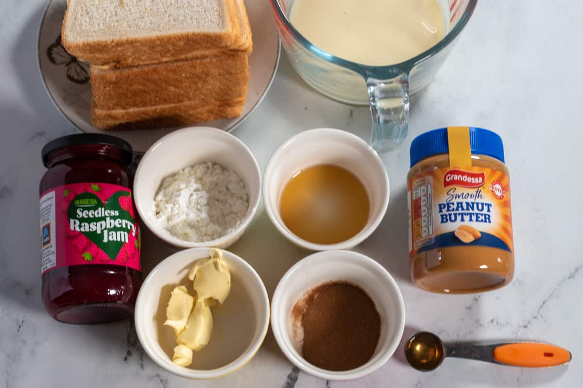 The ingredients needed to make peanut butter and jelly French toast laid out over a white, marble background. 