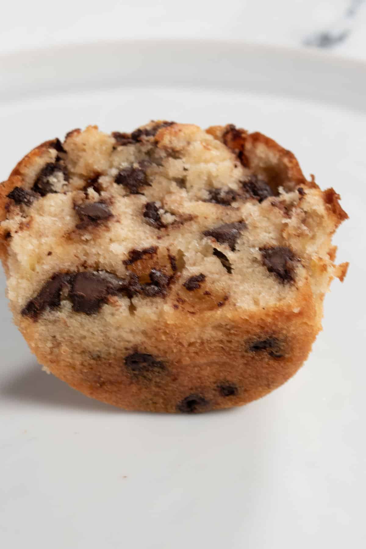 The muffin that is cut in half on a white plate. You can see the insides.  It is fluffy and there are lots of chocolate chips. 