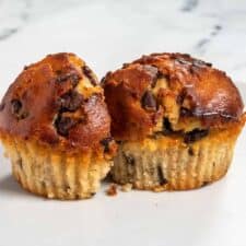 A shot of two vegan peanut butter muffins. One is sliced in half. They have chocolate chips inside.