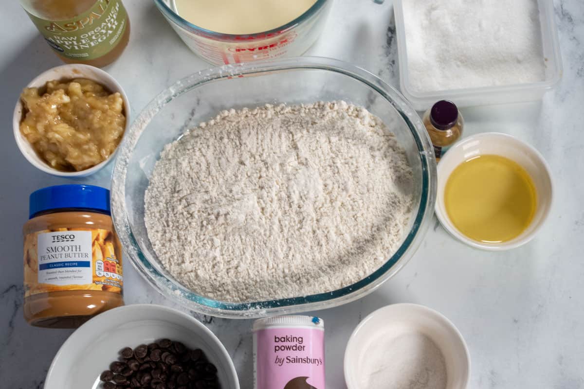 The ingredients needed to make vegan peanut butter muffins laid out over a white, marble background. 