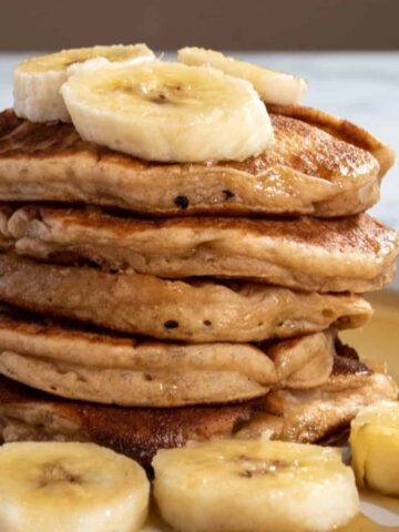A stack of vegan banana protein pancakes. Decorated with maple syrup and chopped bananas.