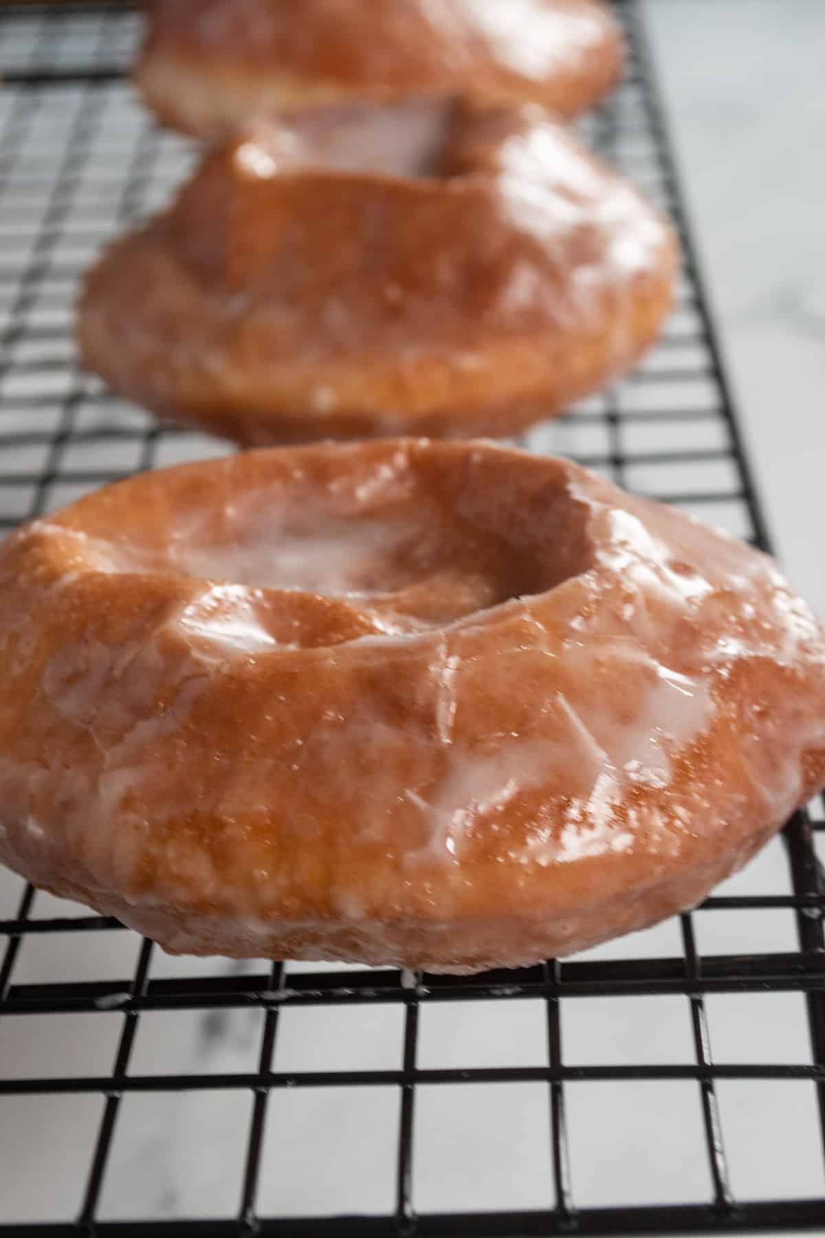 Glazed donuts sat in a line on a wire rack.