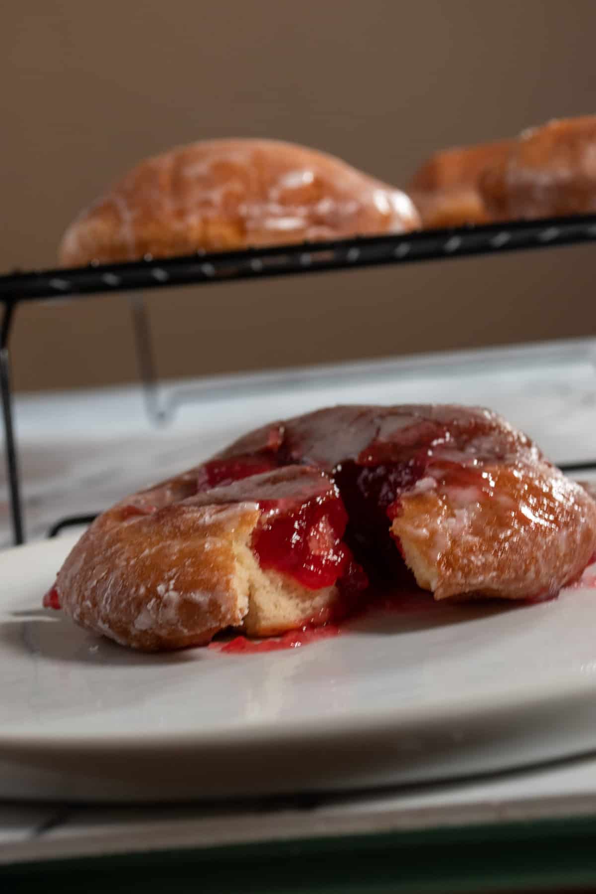 A low shot of my raspberry filled donuts. The one in the foreground is filled but the ones in the background sit on a wire racked unfilled.