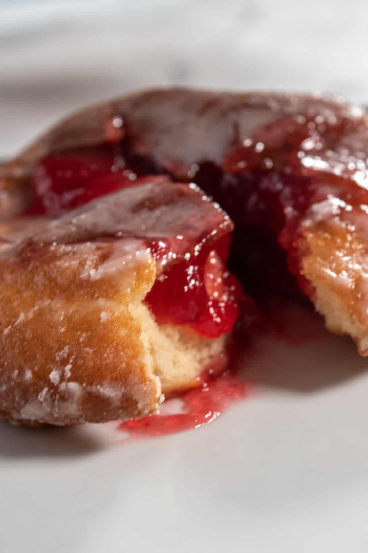 A close up shot of a raspberry filled donut. Lots of jelly oozing out. 
