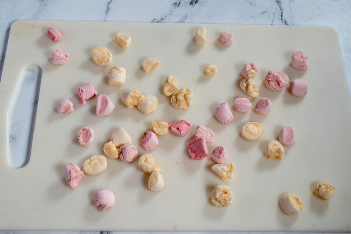 Pink and white vegan marshmallows on a chopping board after being chopped. 