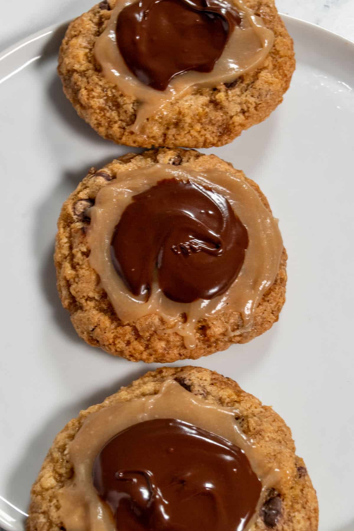 Three vegan twix cookies, on a white plate. They are lined up vertically. 