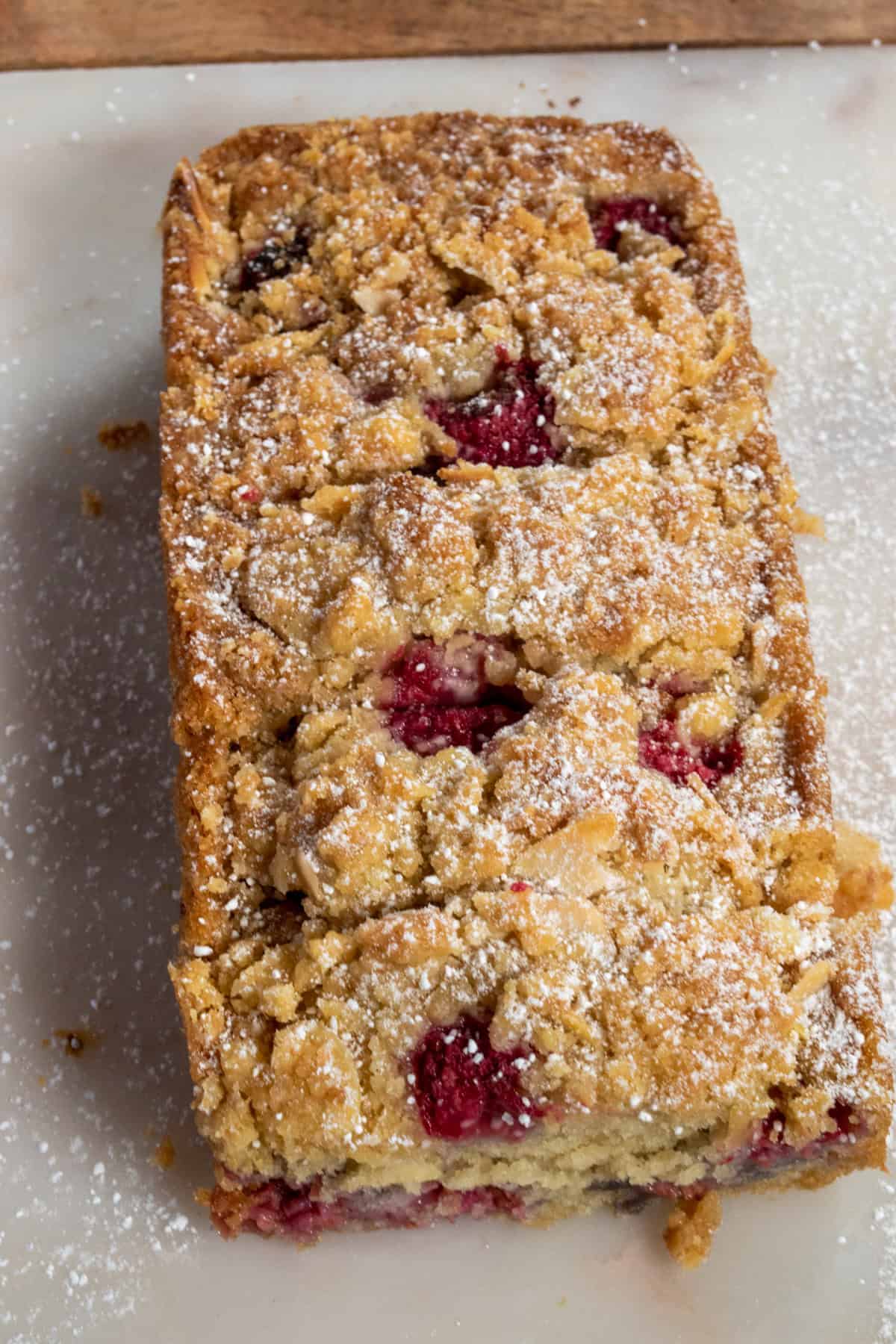 A whole loaf of my almond raspberry cake sitting on a marble platter with powdered sugar sprinkled over it.  