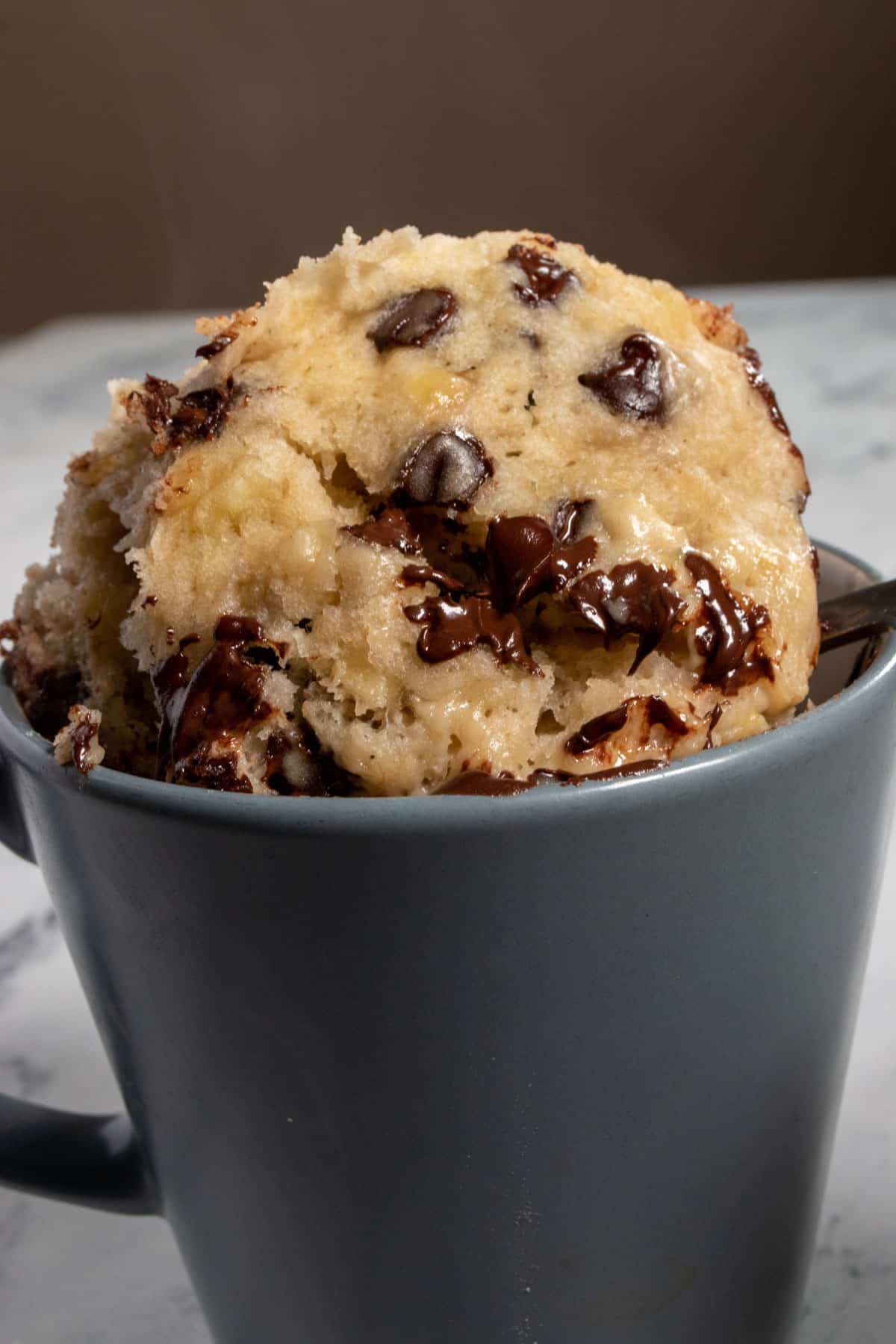 Cake emerging from a matte grey on a spoon. Thew chocolate chips are mostly melted.