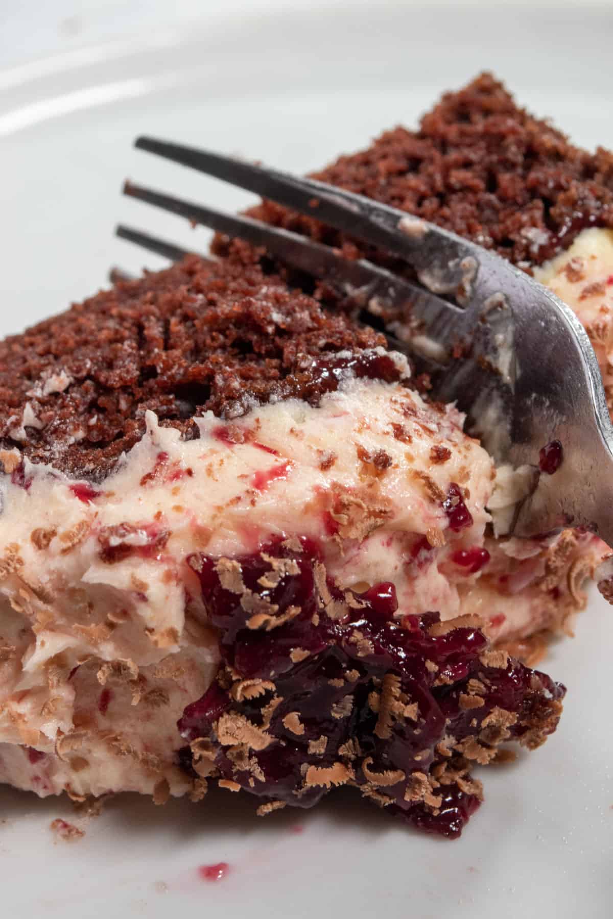 A fork slicing through a thick piece of cake. It has lots of buttercream and cherry compote on it. 