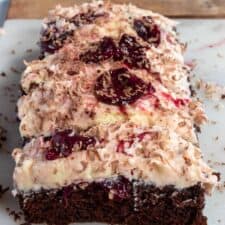 A close up shot of a full vegan black forest cake loaf. Lots of cherries on top making the buttercream pink.