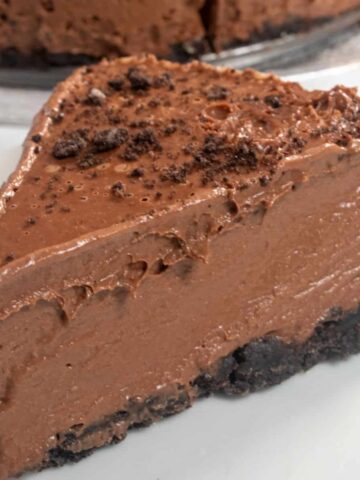 A large slice of vegan chocolate cheesecake on a shiny white plate. It looks silky smooth and has a shine.