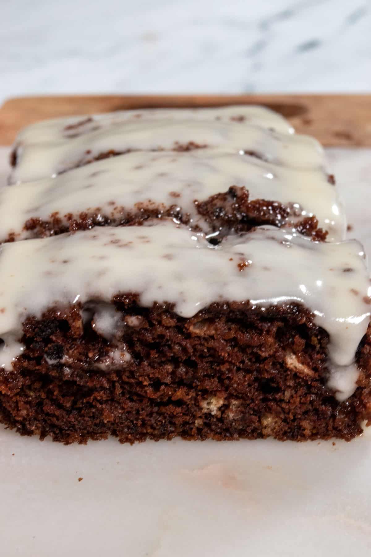 A full loaf of chocolate orange cake with lots of orange on top and dripping down the sides. The front of the cake is sliced off and the texture is moist inside.