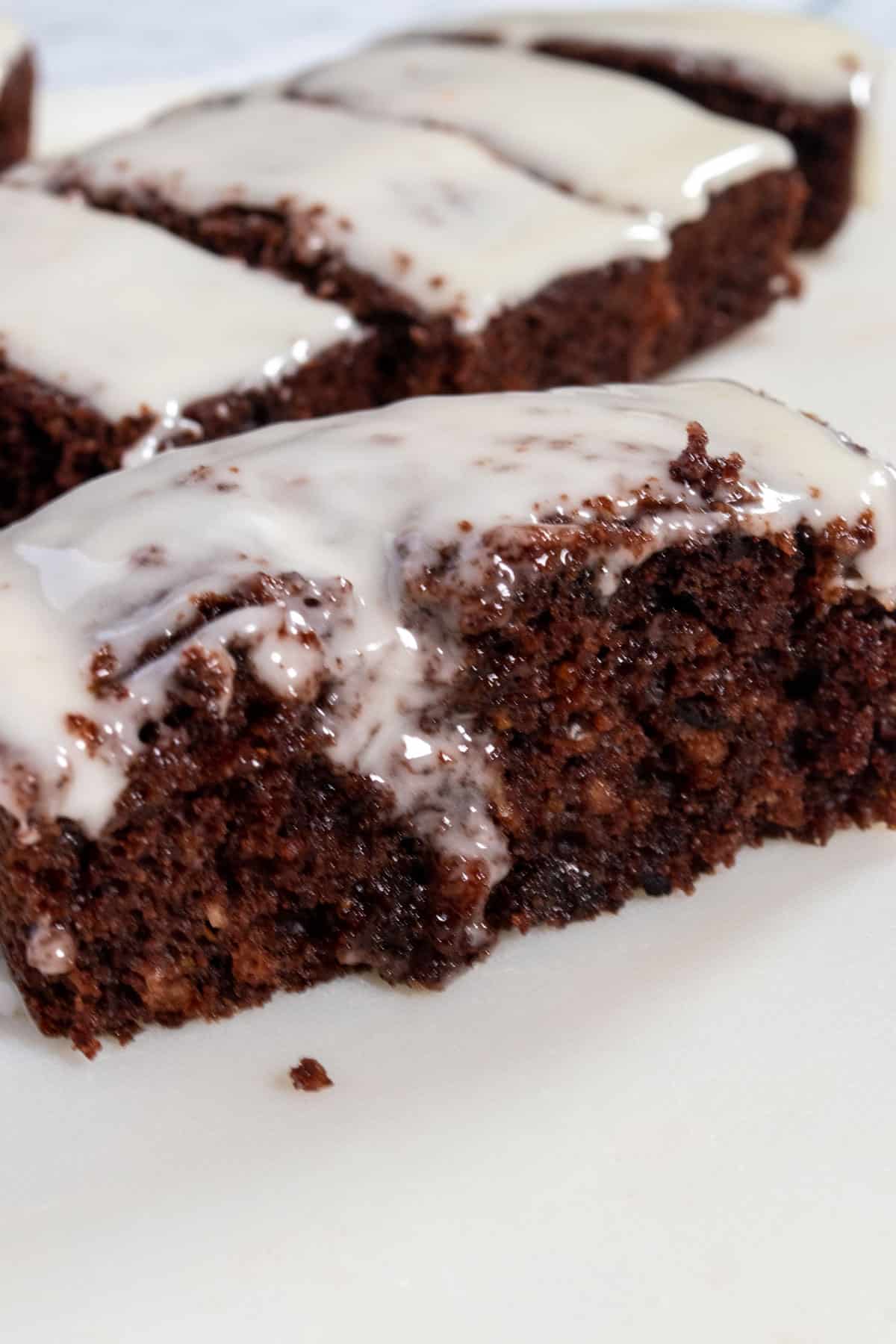 A single, moist slice of vegan chocolate orange cake on a white serving board. The rest of the cake is in the background.