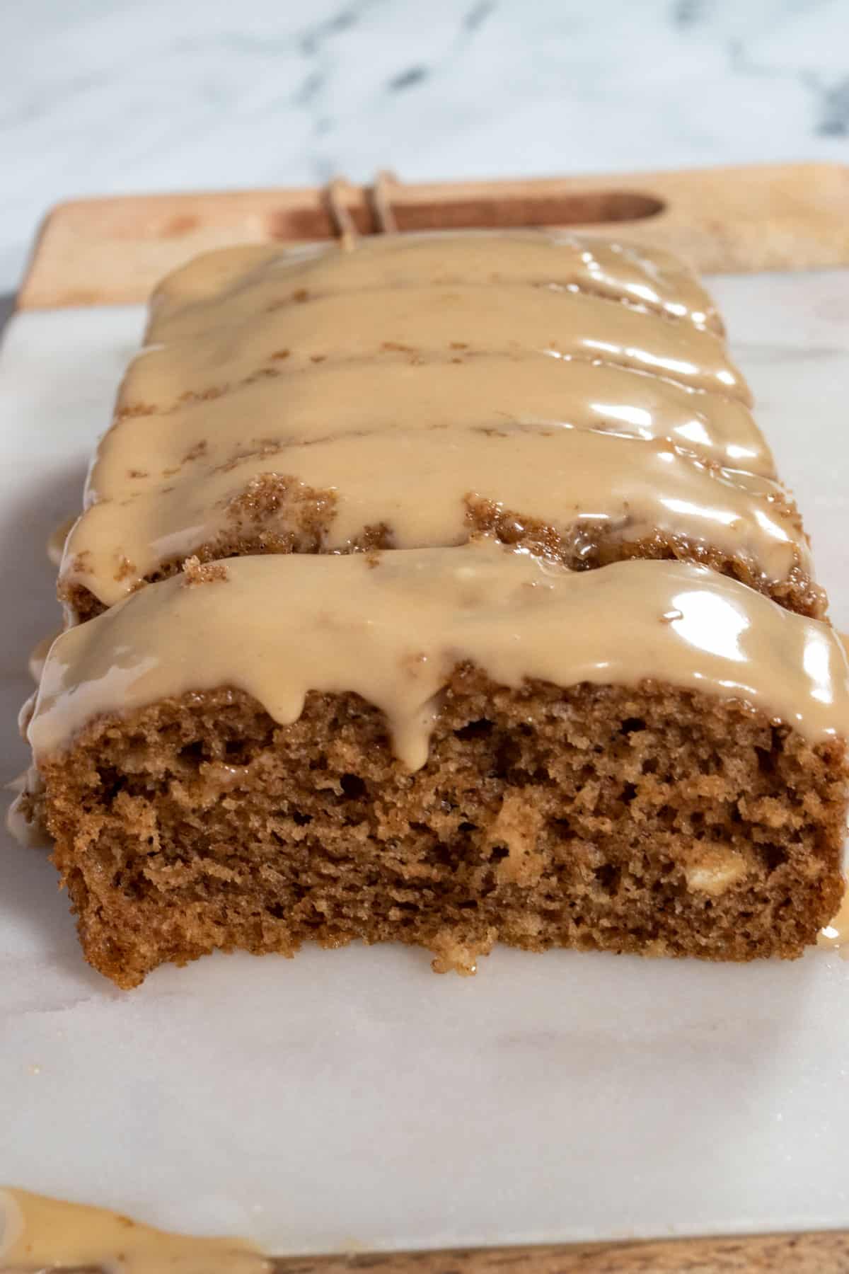 A loaf of vegan gingerbread cake with the front sliced off. The cake looks fluffy and moist on the inside. Biscoff glaze is on top and drips down the sides.