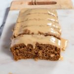 A full loaf of my vegan gingerbread cake, sliced and glazed on a marble platter.