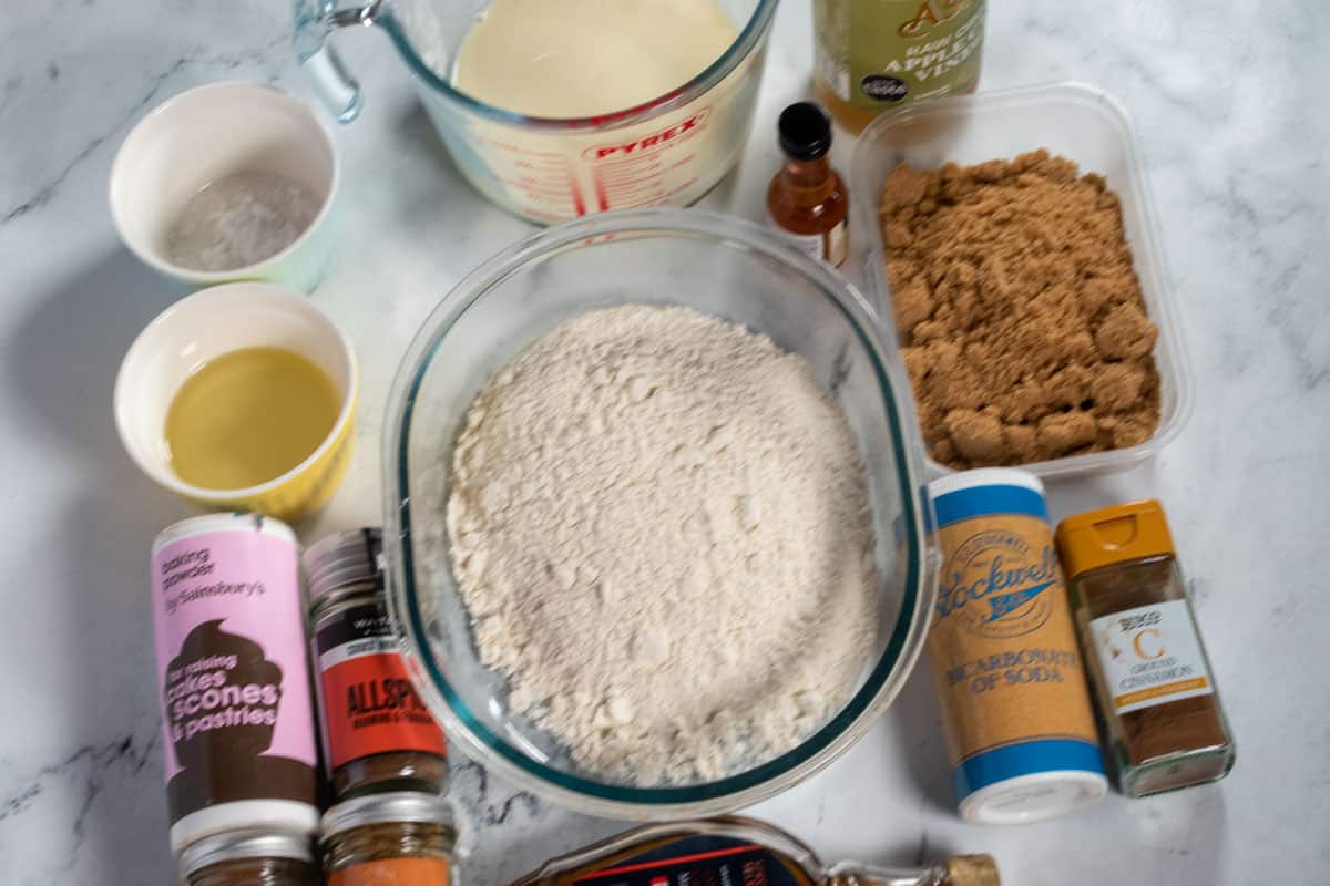 The ingredients needed to make vegan gingerbread cake laid out neatly over a white, marble background. 